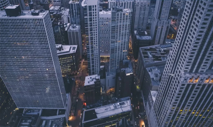 Many large skyscraper exteriors in close proximity at night in city.